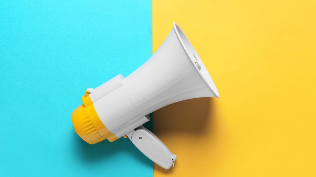 How to Promote Your Small Business Locally | 6 Simple Steps Graphic of a megaphone on a blue and yellow background.